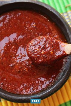 a wooden spoon full of red sauce on top of a pan with a green and yellow table cloth