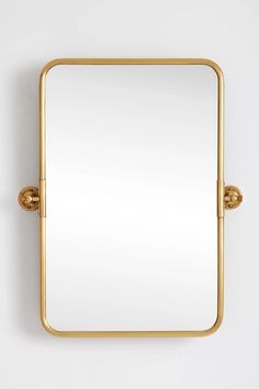 a square mirror mounted on the wall with two brass fittings and a white background