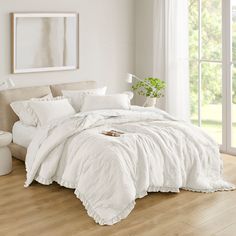 a large white bed sitting in a bedroom next to a window covered in blankets and pillows