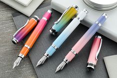 four different colored fountain pens sitting on top of a desk next to a laptop computer