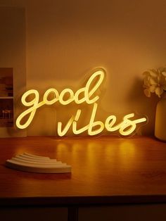 a neon sign that says good vibes on top of a wooden table next to a vase with flowers