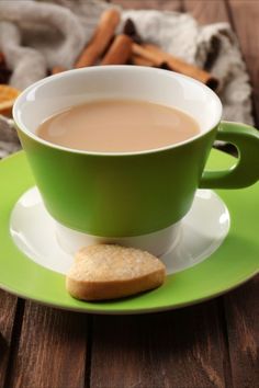 a cup of coffee and some cookies on a green saucer with cinnamon sticks in the background