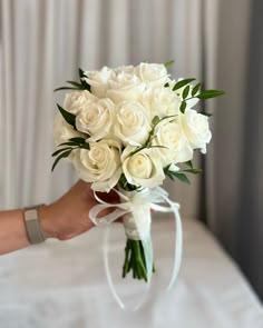 a bouquet of white roses is being held by a woman's hand on a bed