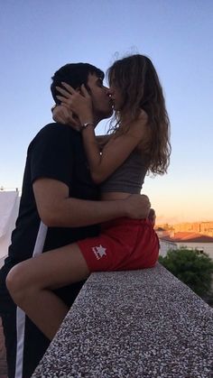 a man and woman kissing while sitting on a ledge