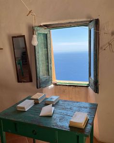 a table with books on it in front of an open window overlooking the ocean and sky