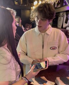 two people standing next to each other at a table with cell phones in their hands