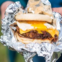 a person holding up a sandwich with cheese and meat on it in aluminum foil wrapper