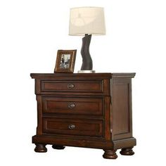 a night stand with two drawers and a lamp on top of the nightstand, against a white background