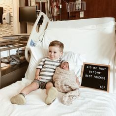 a little boy sitting on top of a hospital bed holding a stuffed animal next to a sign