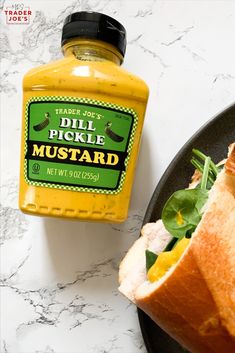 there is a sandwich with mustard on the side and a jar of mustard next to it