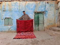 a man standing behind a red rug in front of a blue building