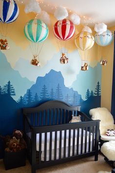 a baby crib in front of a wall with hot air balloons hanging from it