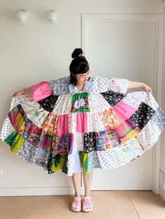 a woman standing in front of a white wall wearing a colorful dress