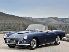 an old blue sports car parked in front of a mountain