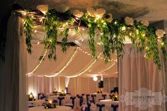 a banquet hall decorated with white flowers and greenery hanging from the ceiling over tables