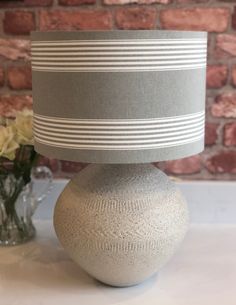 a gray and white striped lamp shade sitting on top of a table next to a vase with flowers