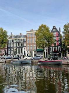 several boats are parked along the water in front of some buildings and trees on either side