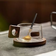 a glass cup with a spoon in it on top of a wooden stand next to glasses