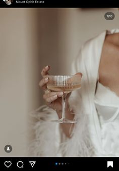 a woman holding a wine glass in her hand while wearing a white shirt and fur coat