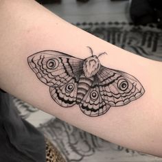 a black and white moth tattoo on the left upper arm, with circles around it