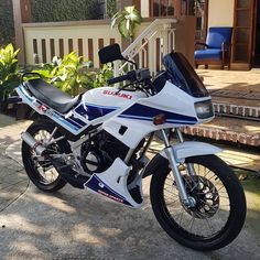 a white and blue motorcycle parked in front of a house next to a wooden deck