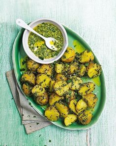 a green plate topped with potatoes covered in pesto next to a bowl of sauce