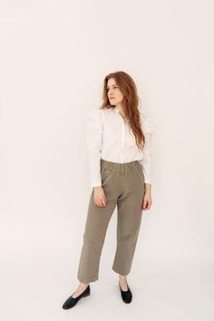 a woman in white shirt and khaki pants with black shoes standing against a white background