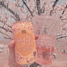 a person holding up two plastic cups in front of a tree with flowers on it