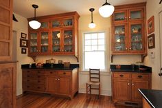 an empty kitchen with wooden cabinets and black counter tops, along with a chair in front of the window