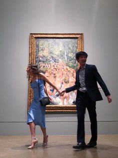 a man and woman holding hands in front of a large painting on display at an art museum