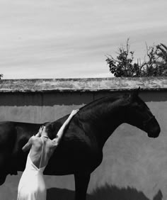 a woman is standing next to a horse in black and white, with her hand on the back of the horse's head