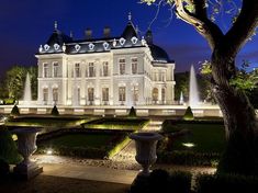 a large white building with fountains in front of it at night, surrounded by greenery and trees