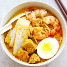 a bowl of soup with shrimp, tofu and egg on the side next to chopsticks