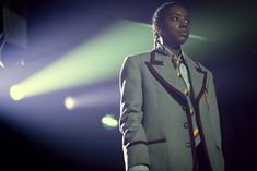 a man in a coat and tie standing on stage with his hands behind his back