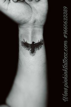 a black and white photo of a person holding their hand up with a bird tattoo on it