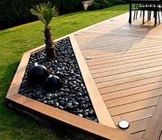 a wooden deck with black rocks and a palm tree in the center is surrounded by green grass