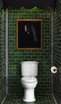 a white toilet sitting in a bathroom next to a green tiled wall with a painting on it