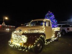 an old truck decorated with lights and a christmas tree