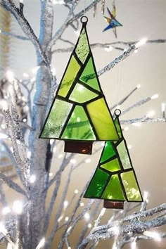 a stained glass christmas tree ornament hanging from a silver tree with white lights