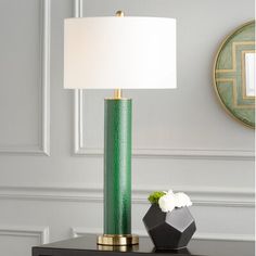 a green lamp sitting on top of a table next to a vase with white flowers