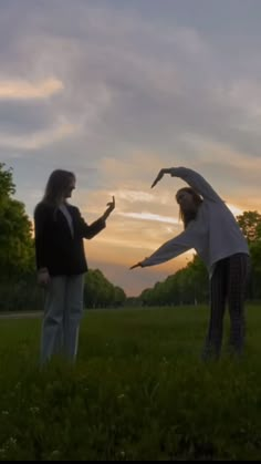 two people standing in the grass with their arms spread out and one person reaching for something