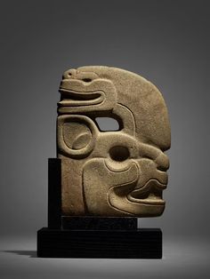 an ancient mask is displayed on a black stand in front of a gray background,