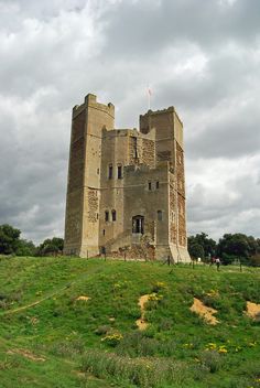 an old stone castle sitting on top of a lush green hillside under a cloudy sky