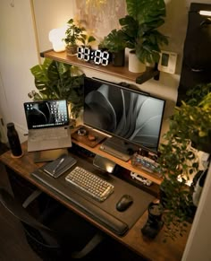 a computer desk with a laptop, keyboard and monitor on it next to some plants