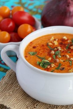 a white bowl filled with soup next to some tomatoes and other vegetables on a table