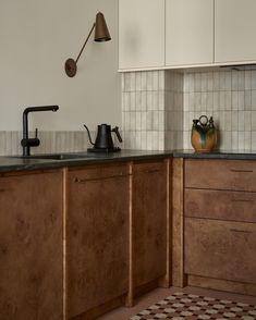 a kitchen with wooden cabinets and black counter tops, an old fashioned tea kettle on the stove