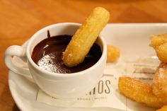 two churro sticks are in a cup and sauce is on the plate next to it