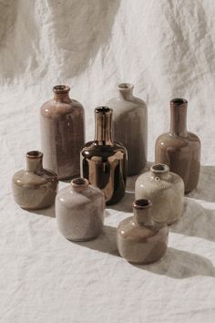 there are many different vases sitting on the white sheeted tablecloth, and one is empty