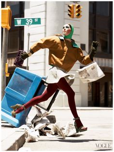 a woman in red tights and green head scarf is walking past a trash can