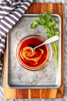 a glass bowl filled with sauce and garnished with parsley on a wooden cutting board